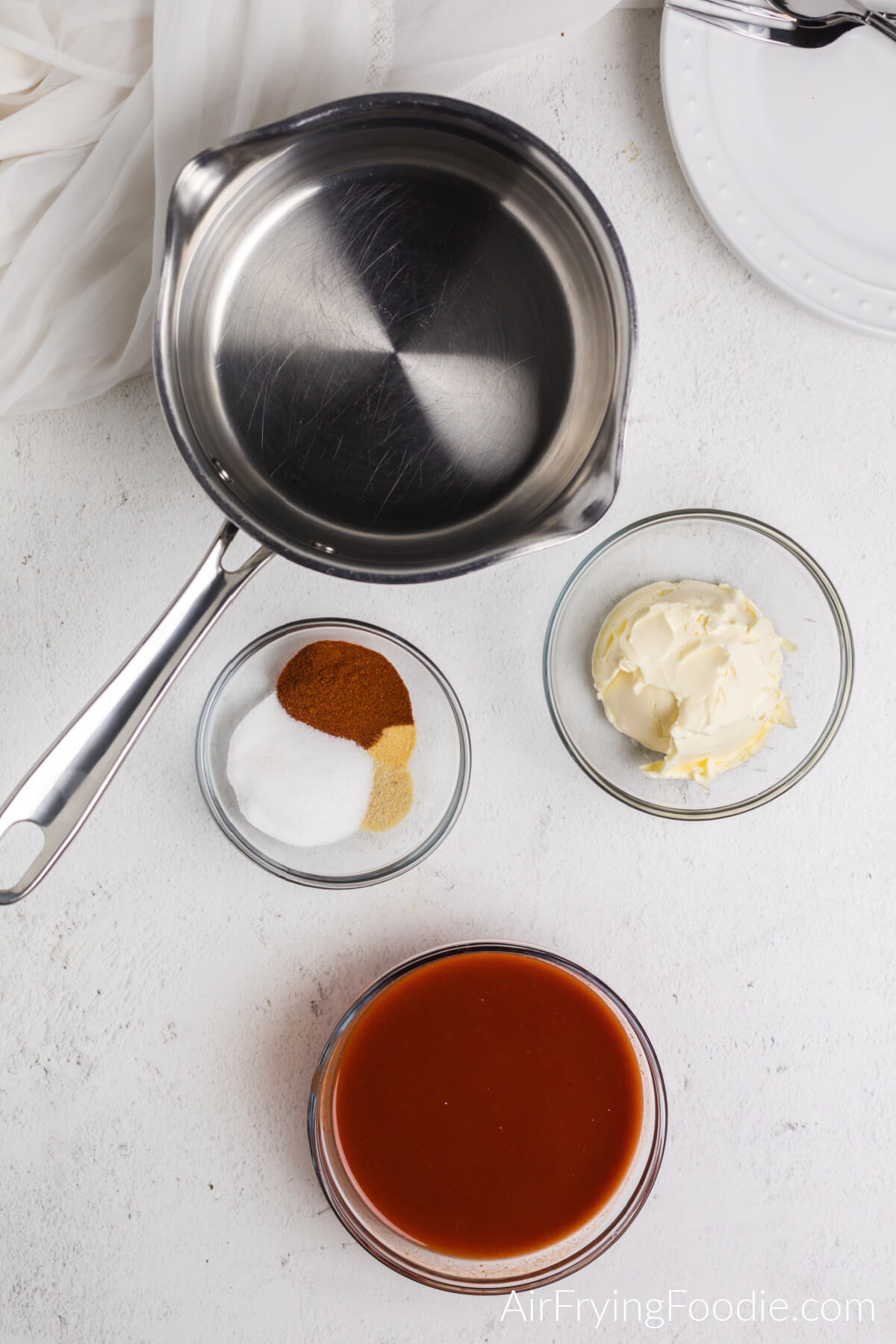 Ingredients needed to make the homemade wing sauce: sauce pan, hot sauce in a bowl, seasonings in a bowl, and margarine or butter in a bowl. 