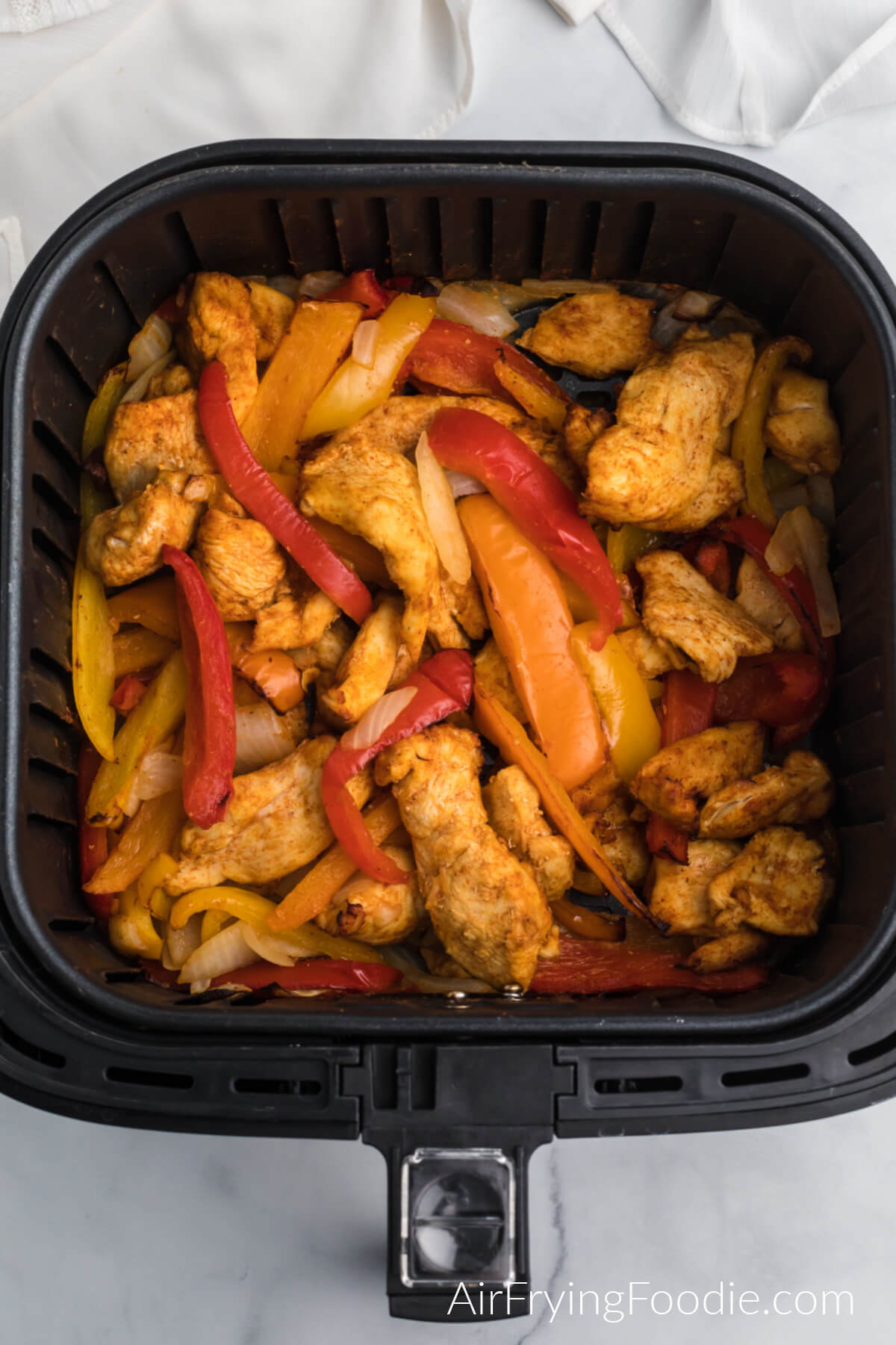 Air fried chicken fajita meat, peppers, and onions in the basket of the air fryer. 