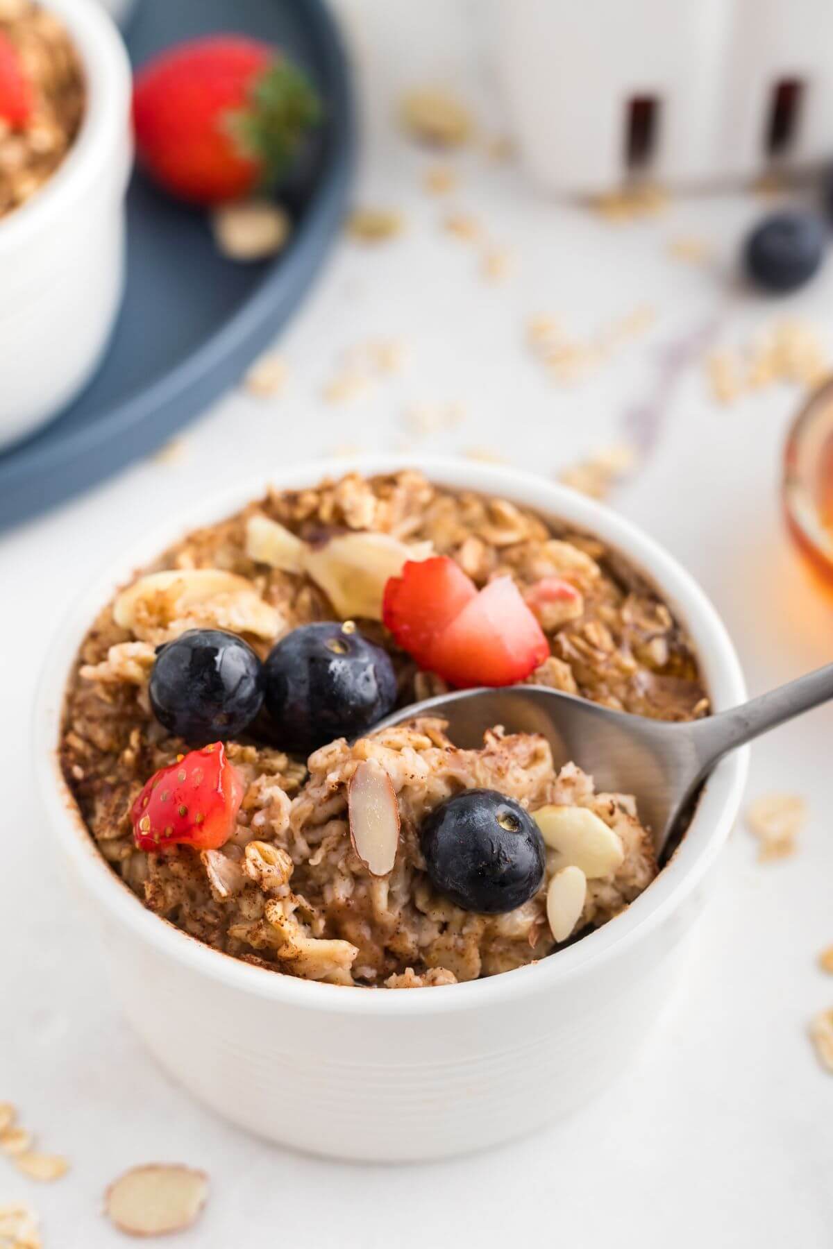 Moist oatmeal in a white ramekin topped with fruit and slivered almonds. 