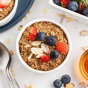 Golden brown oatmeal in a white ramekin topped with fruit and slivered almonds.
