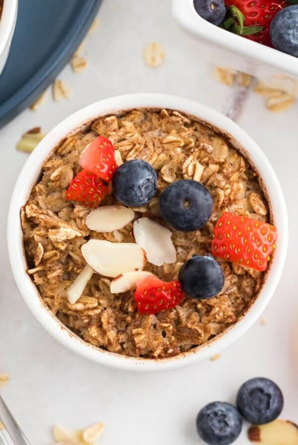 Golden brown oatmeal in a white ramekin topped with fruit and slivered almonds.