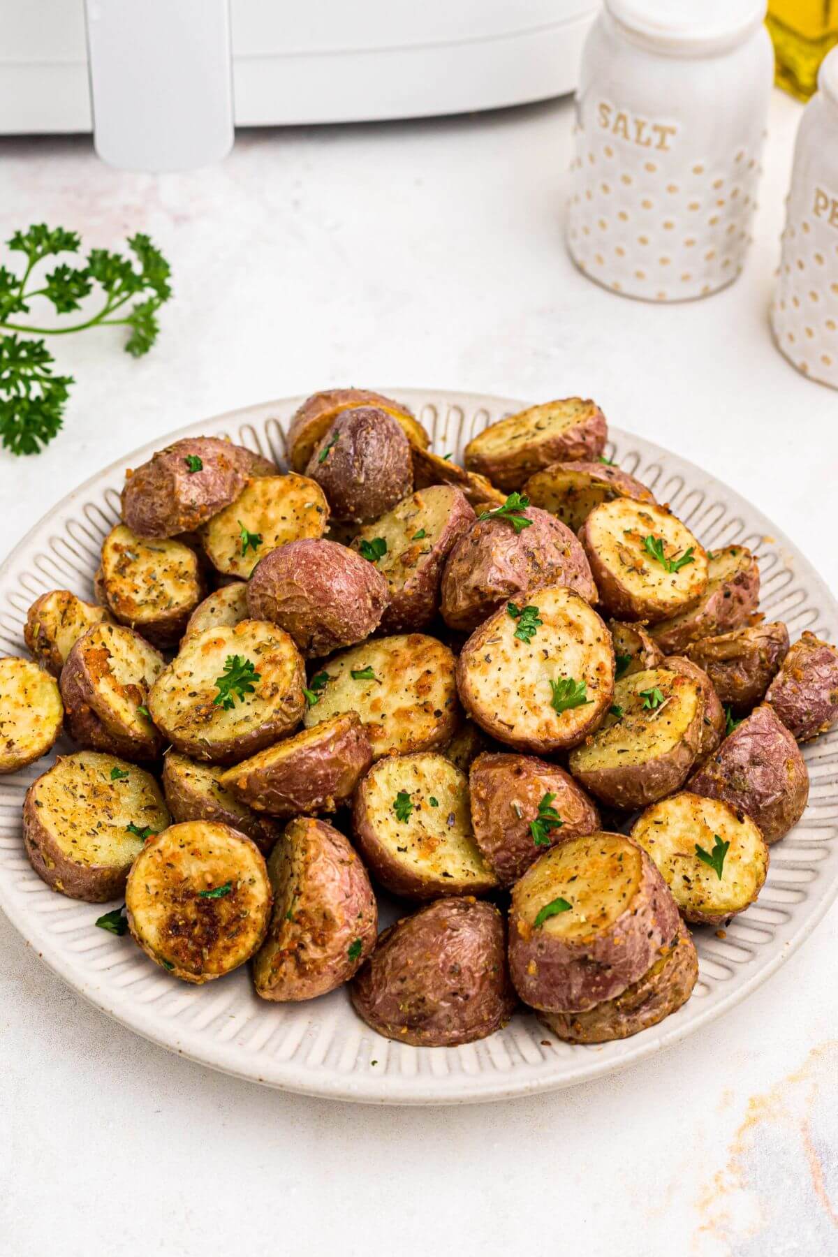 Baby red potatoes sliced in half and cooked until golden brown with seasonings, stacked on a white plate. 