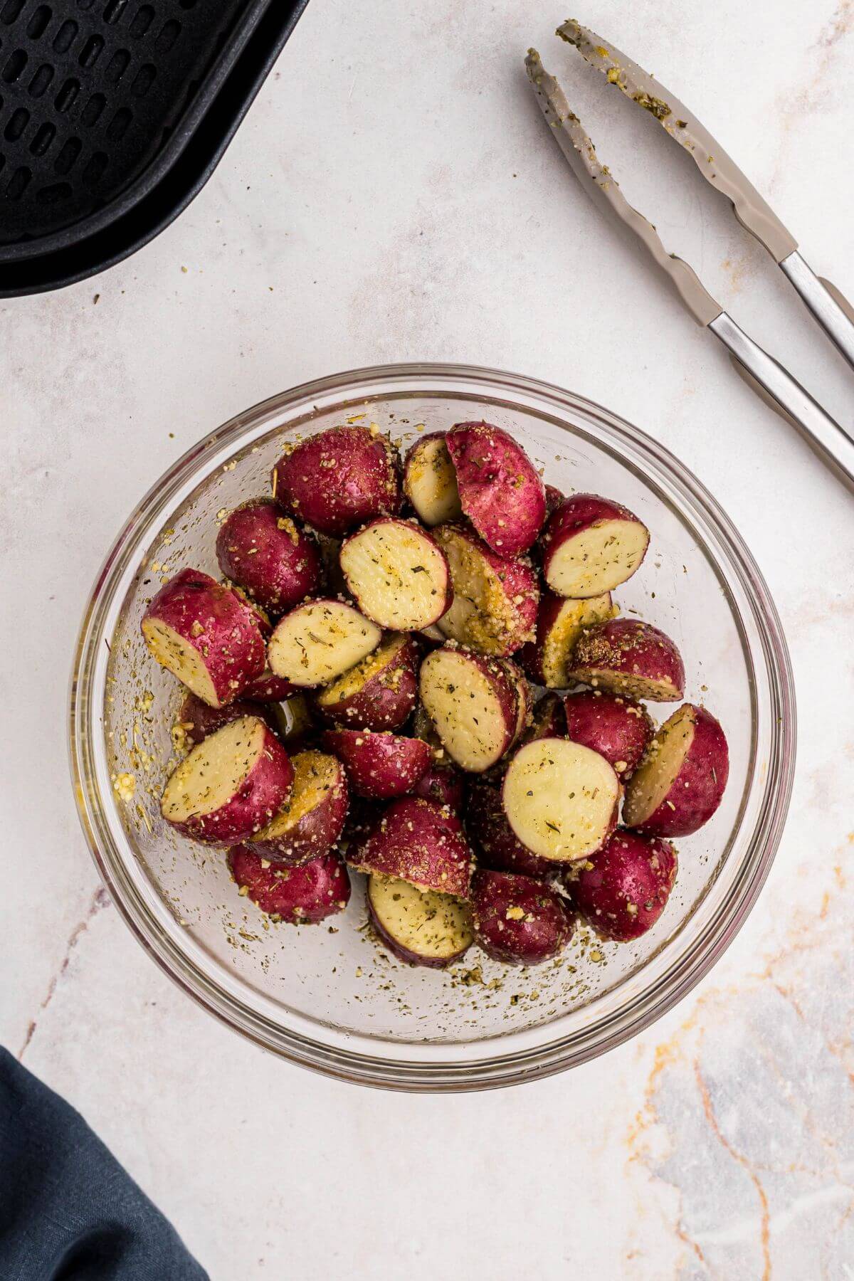 Red baby potatoes in a clear glass bowl after being tossed with olive oil, seasonings, and parmesan cheese. 