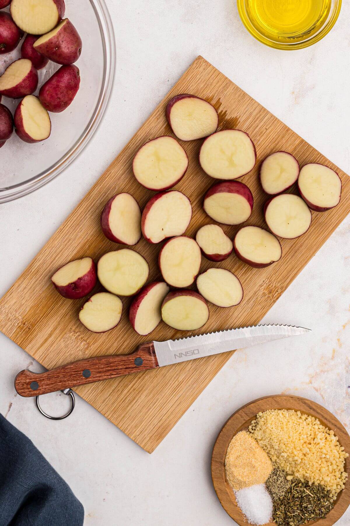 Baby red potatoes being cut in half on a wooden cutting board. 