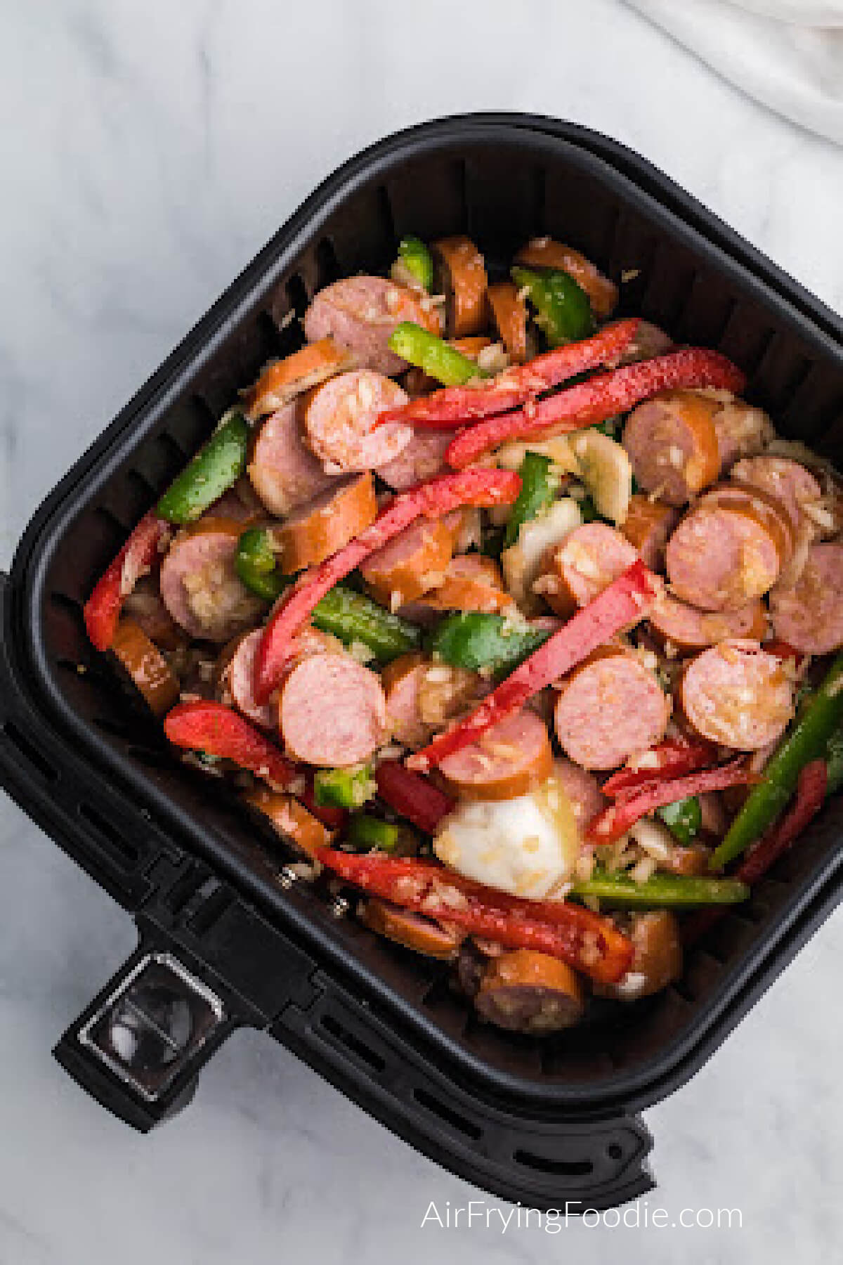 sausage, onion, and peppers added to the basket of the air fryer and ready to cook. 