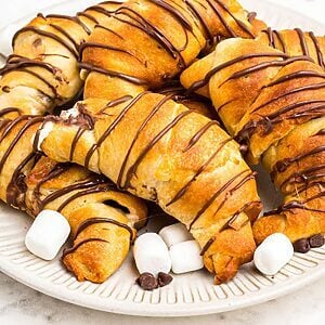 Golden air fryer s'mores crescent rolls stacked on a plate with mini marshmallows and chocolate chips, stacked on a plate.