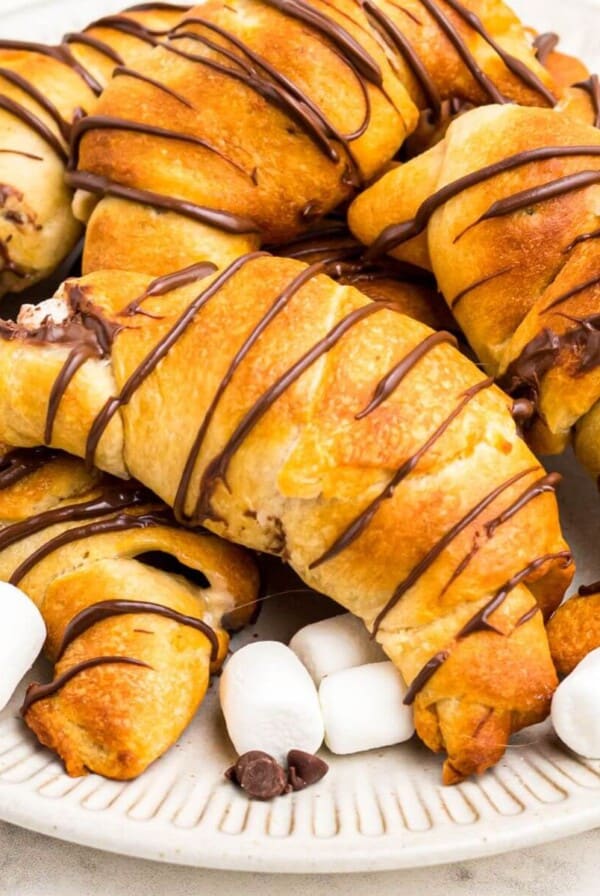 Golden air fryer s'mores crescent rolls stacked on a plate with mini marshmallows and chocolate chips, stacked on a plate.