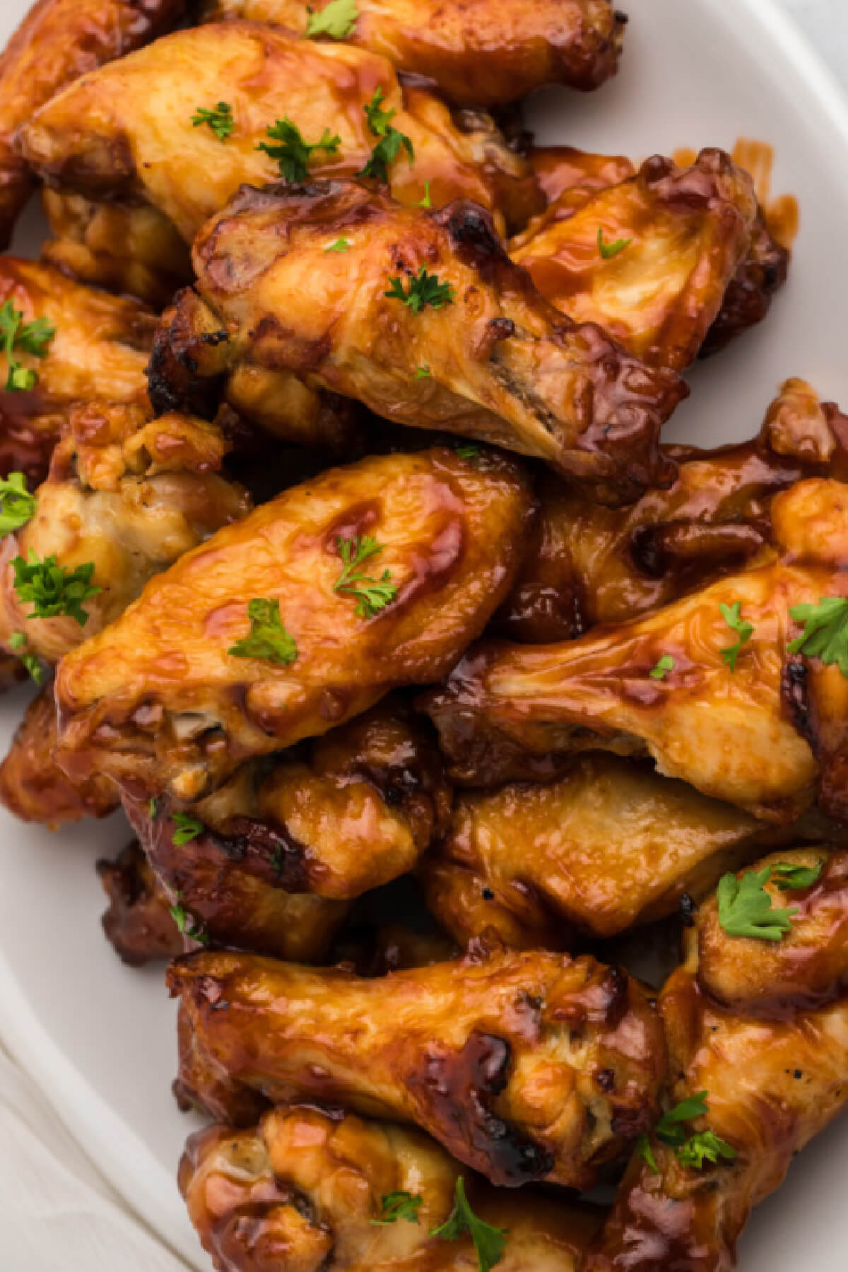 bbq chicken wings made in the air fryer and topped with fresh parsley and served on a white plate. 