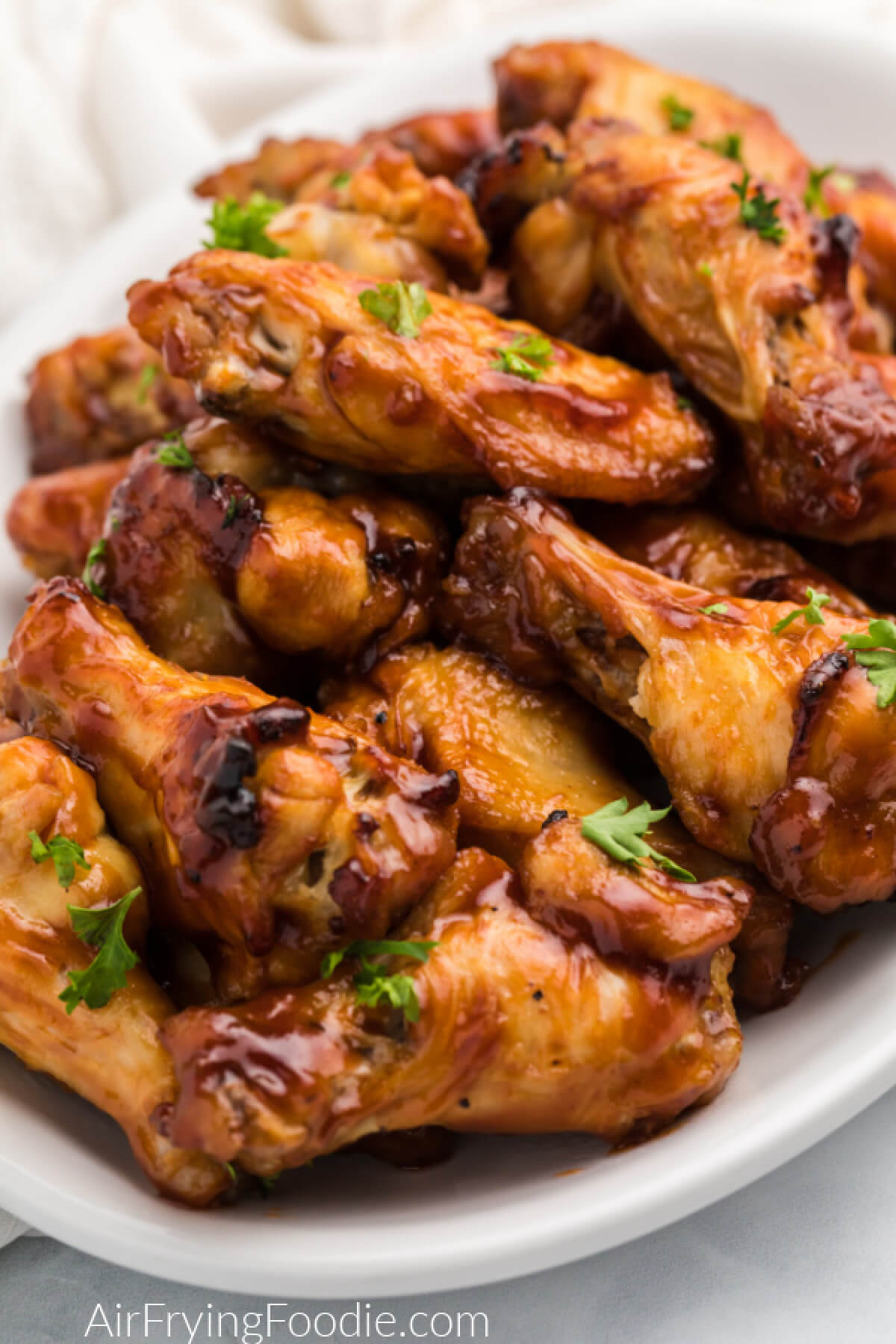 BBQ chicken wings made in the air fryer topped with fresh parsley and served on a white plate. 