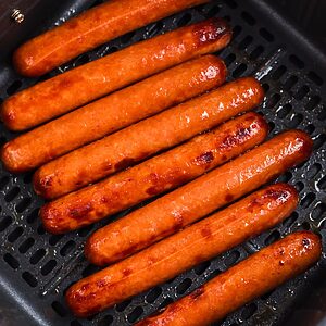 Juicy plump hot dogs in the air fryer basket after being cooked.