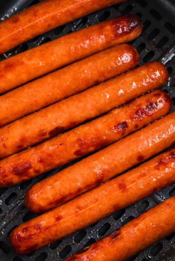 Juicy plump hot dogs in the air fryer basket after being cooked.