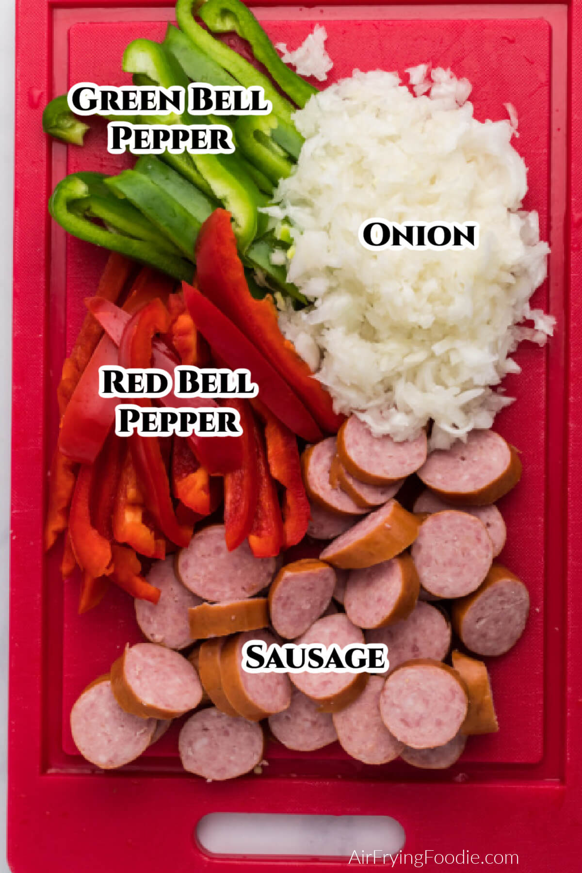 Red cutting board with sliced bell peppers, sausage, and diced onions. 