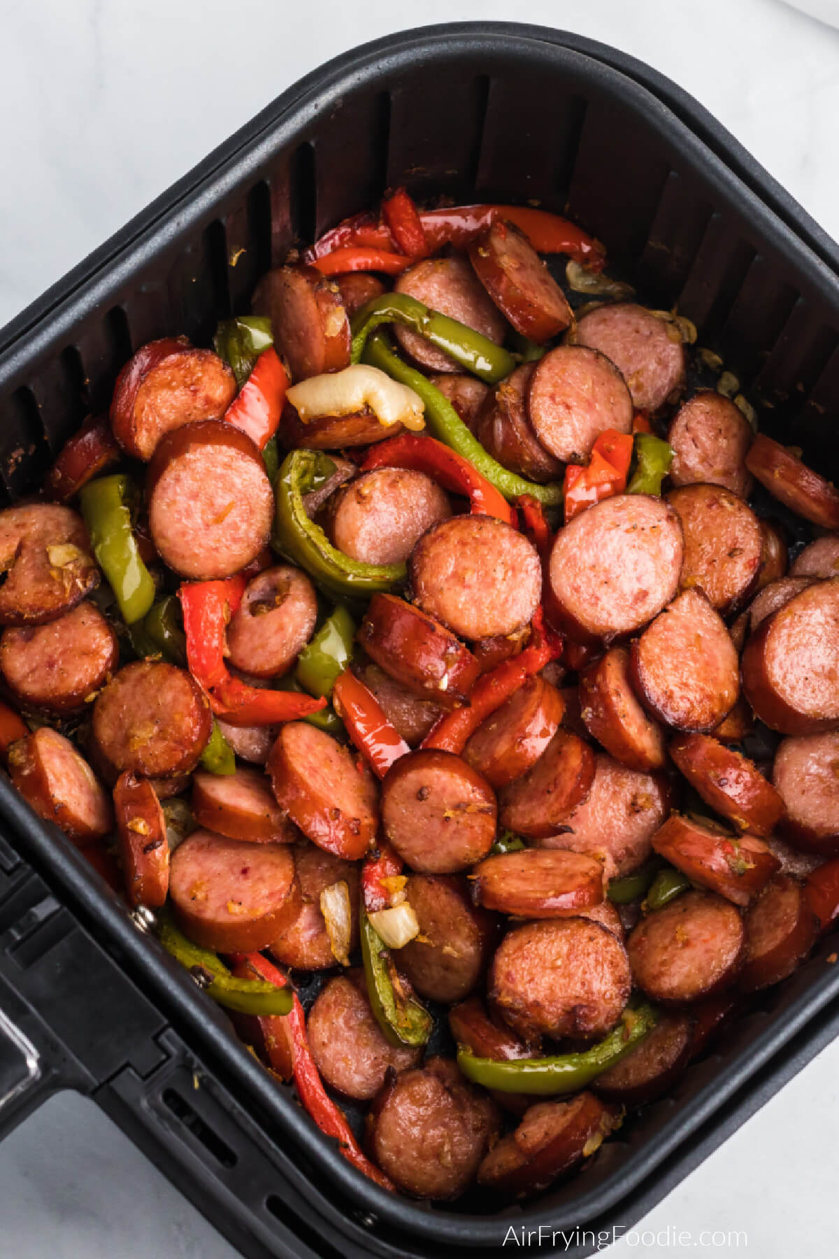 Seasoned sausage and peppers in air fryer basket, ready to serve.