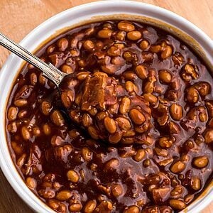 Golden juicy baked beans in a white ramekin with a spoon serving.