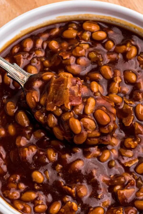 Golden juicy baked beans in a white ramekin with a spoon serving.