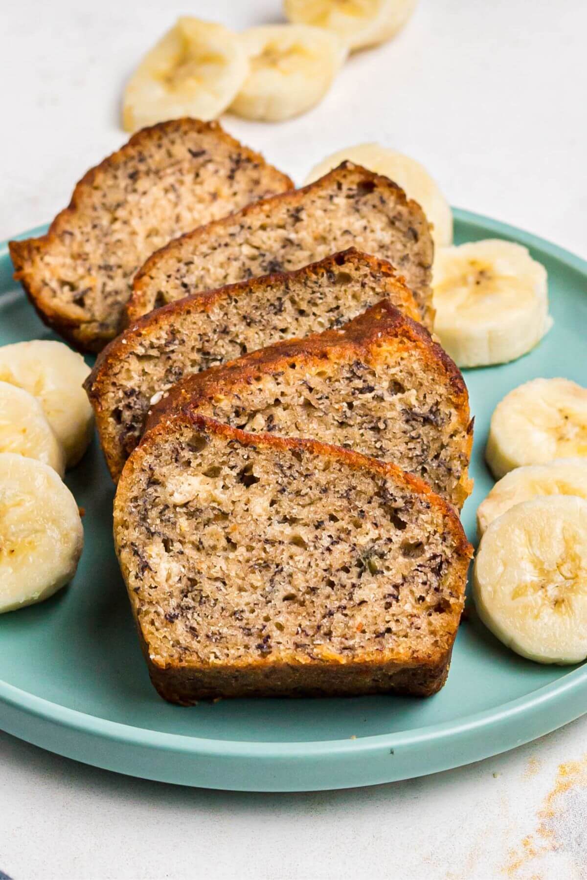 Golden brown baked banana bread sliced on a light green plate with slices of banana on the plate. 