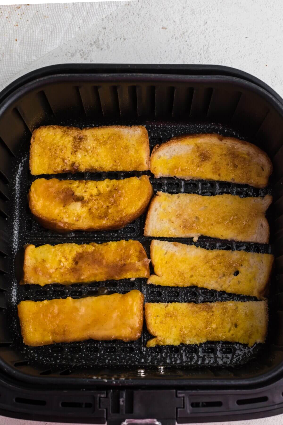 Dipped bread sliced placed in a single layer in the air fryer basket. 