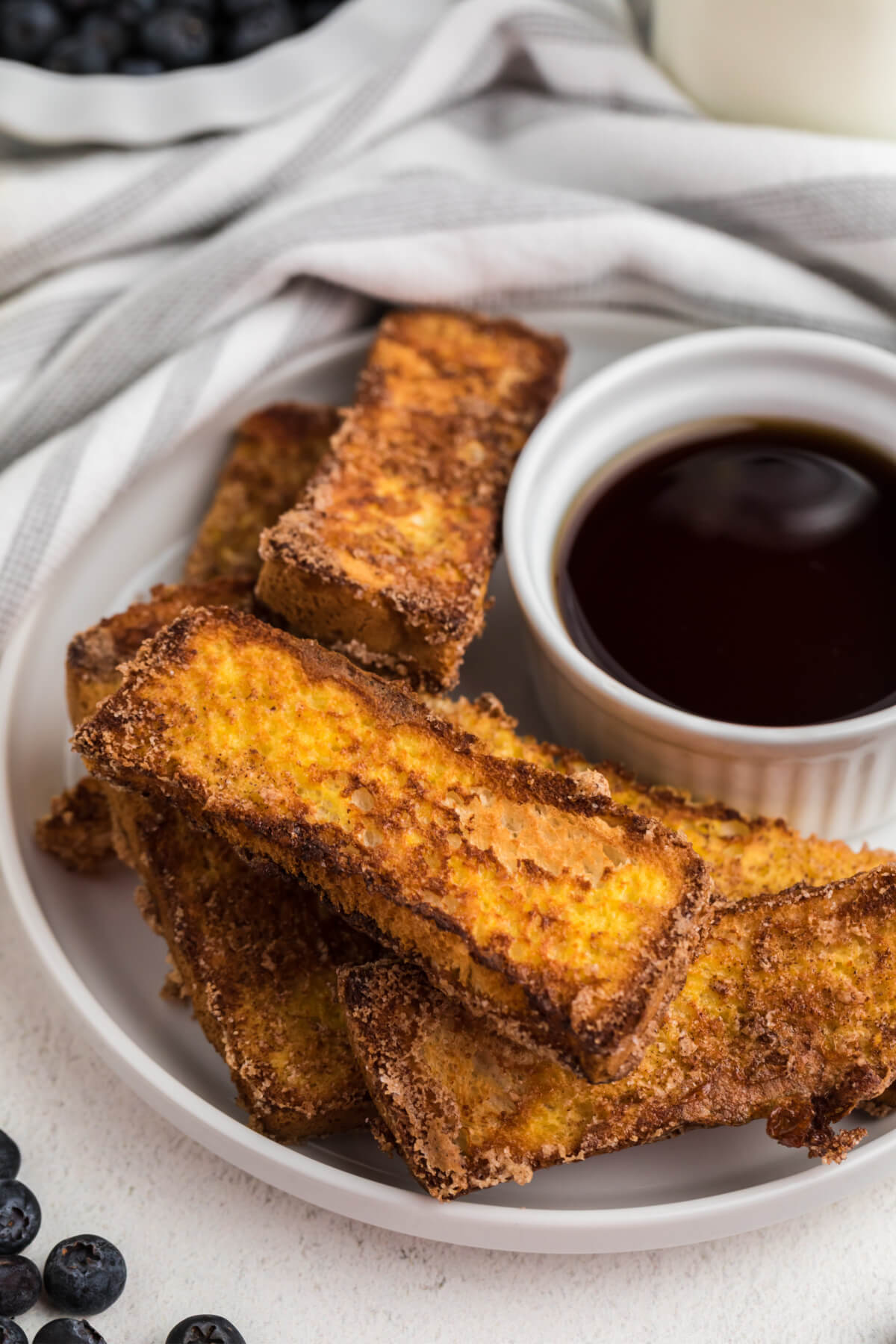 french toast sticks made in air fryer basket served on a a white plate with syrup for dipping. 