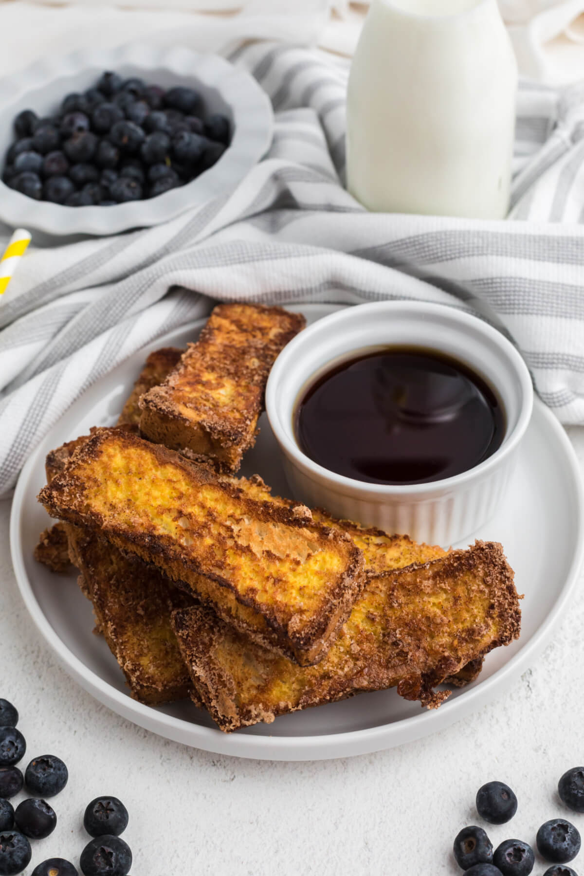 French toast sticks made in the air fryer, served on a white plate with a bowl of syrup for dipping. 