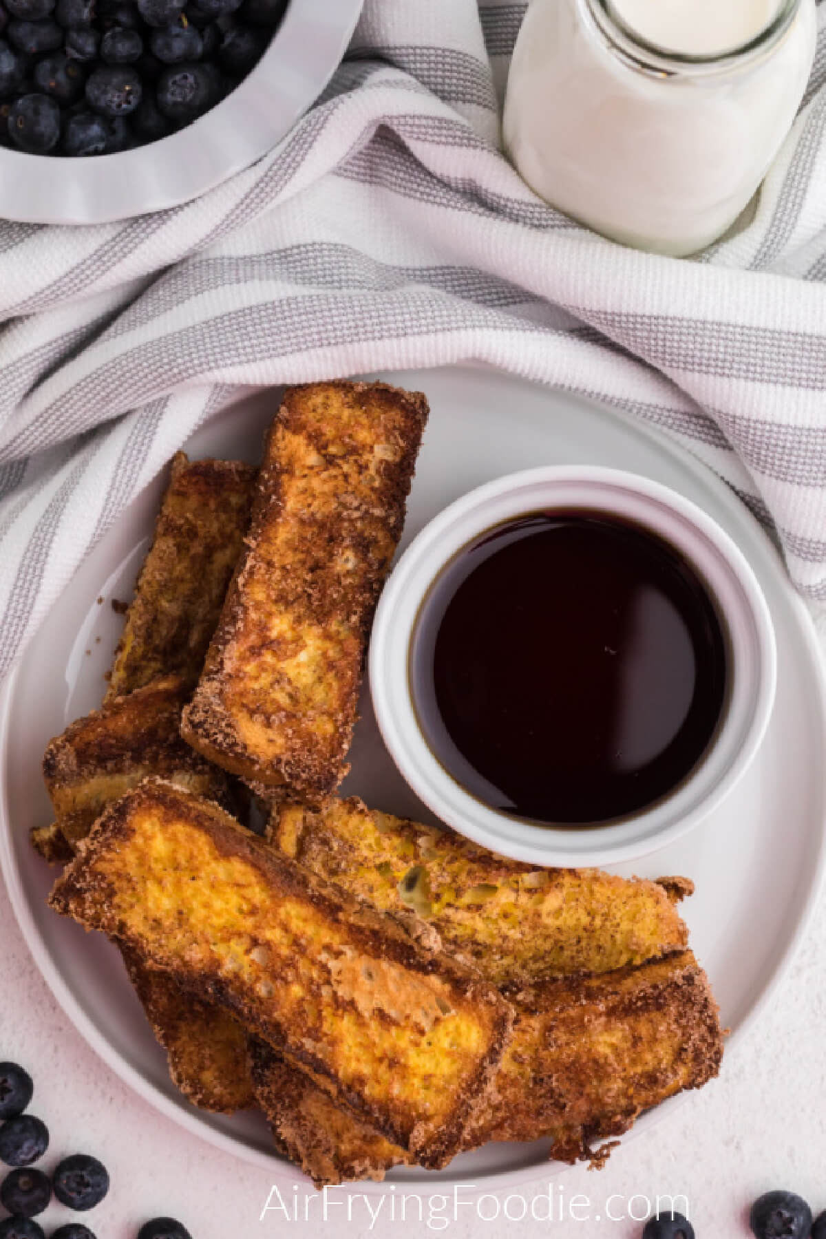 Overhead shot of french toast sticks made in the air fryer with a side of syrup for dipping. 