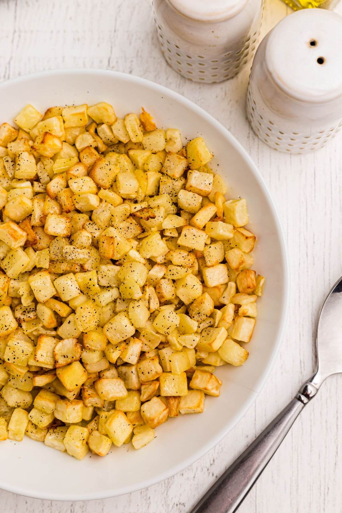 Golden seasoned diced potatoes in a white bowl with a serving spoon. 