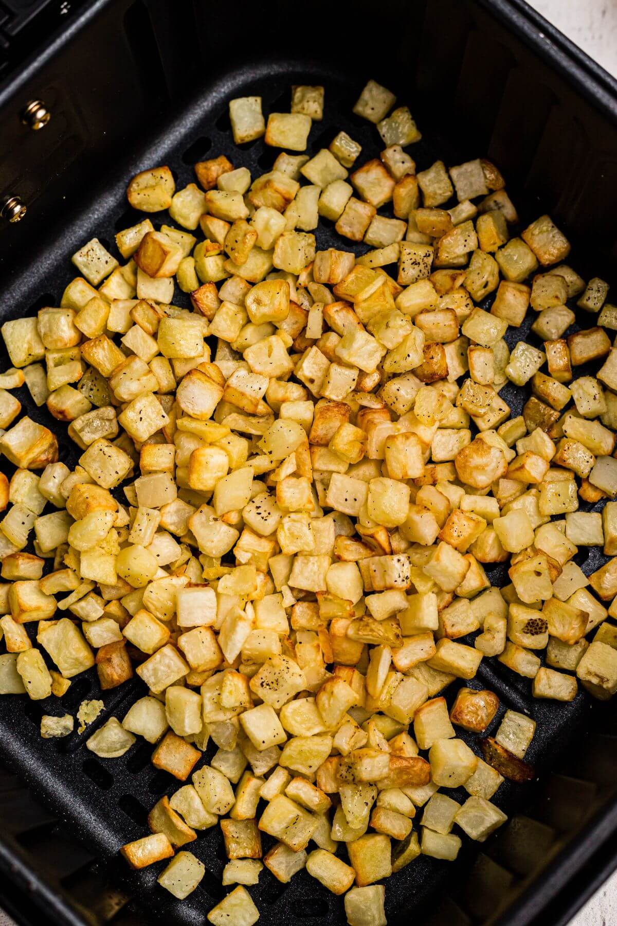 Golden brown and crispy diced potatoes after being cooked in the air fryer basket. 