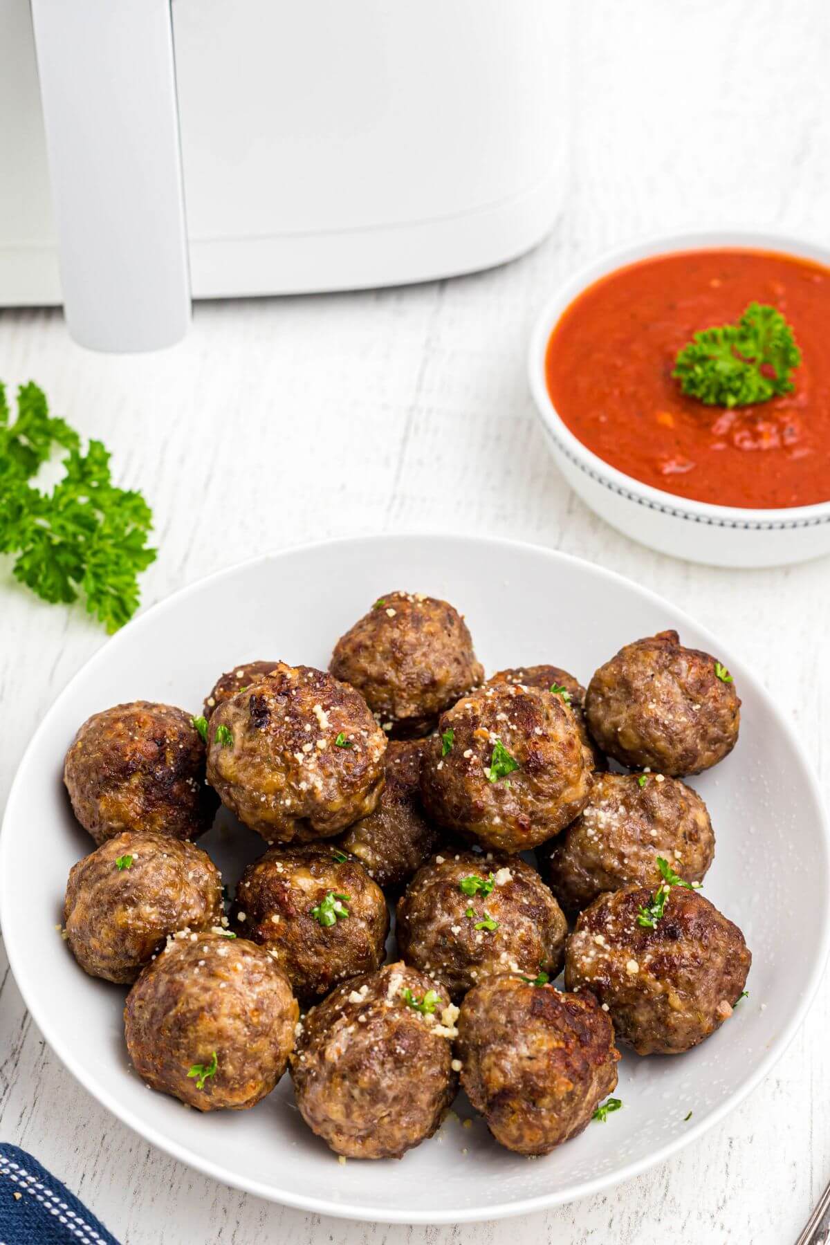 Golden brown juicy meatballs stacked in a white bowl in front of red sauce and the air fryer. 