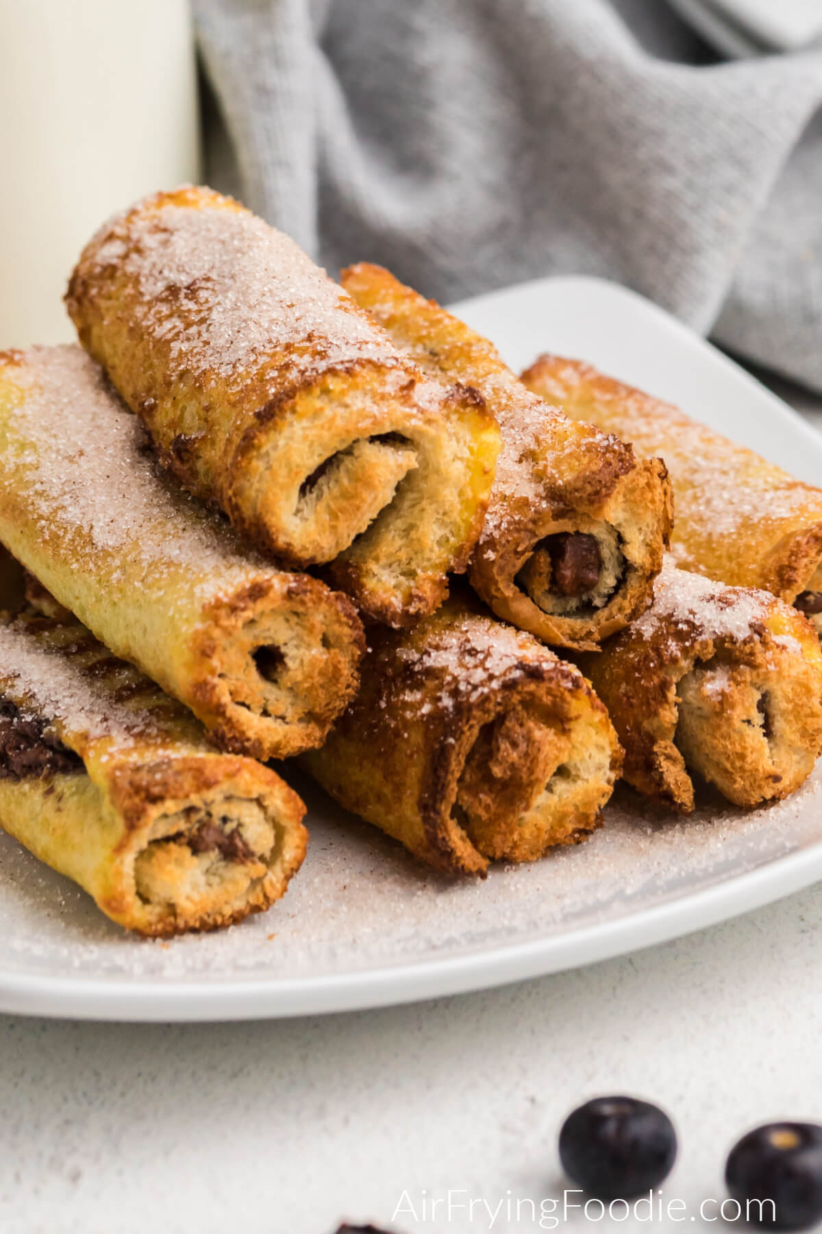 air fryer nutella french toast roll ups on a white olate topped with cinnamon and sugar.