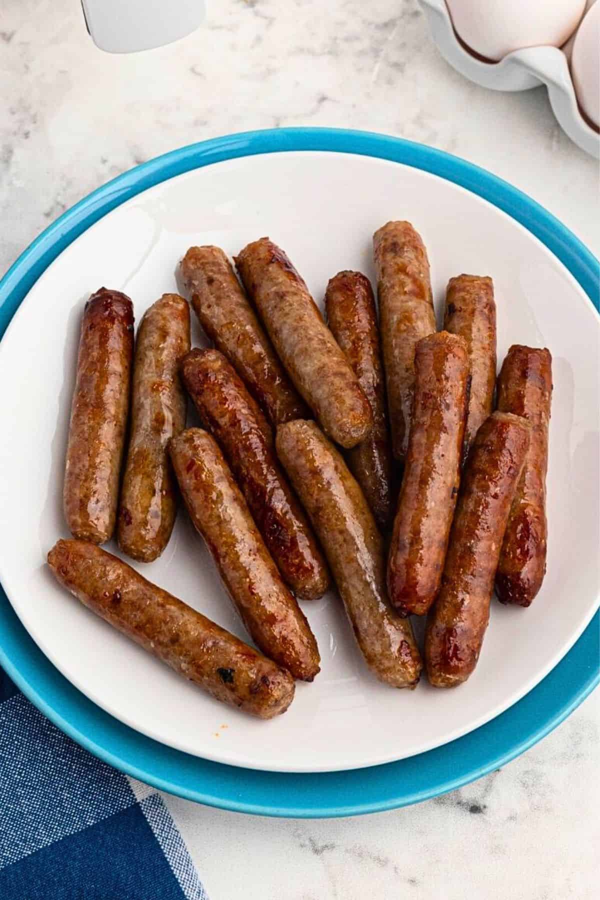 White plate filled with crispy, golden brown, cooked sausage links, on a marble table in front of an air fryer.