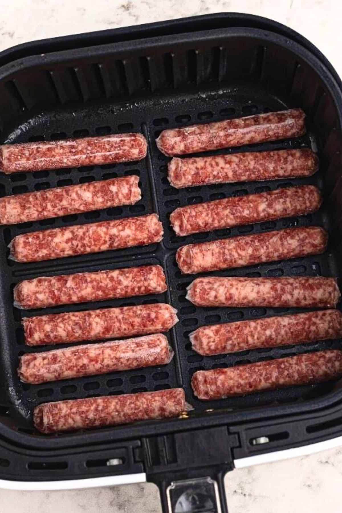 Uncooked sausage links placed side by side in the air fryer basket. 