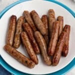 White plate filled with crispy, golden brown, cooked sausage links, on a marble table in front of an air fryer.