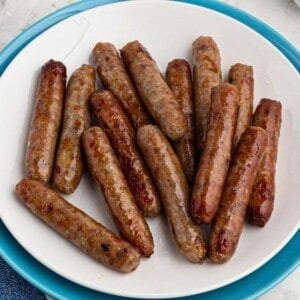 White plate filled with crispy, golden brown, cooked sausage links, on a marble table in front of an air fryer.