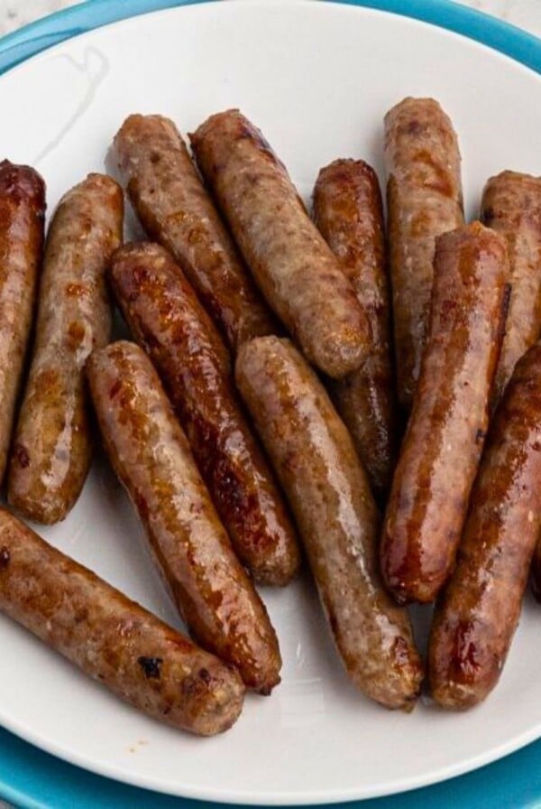 White plate filled with crispy, golden brown, cooked sausage links, on a marble table in front of an air fryer.