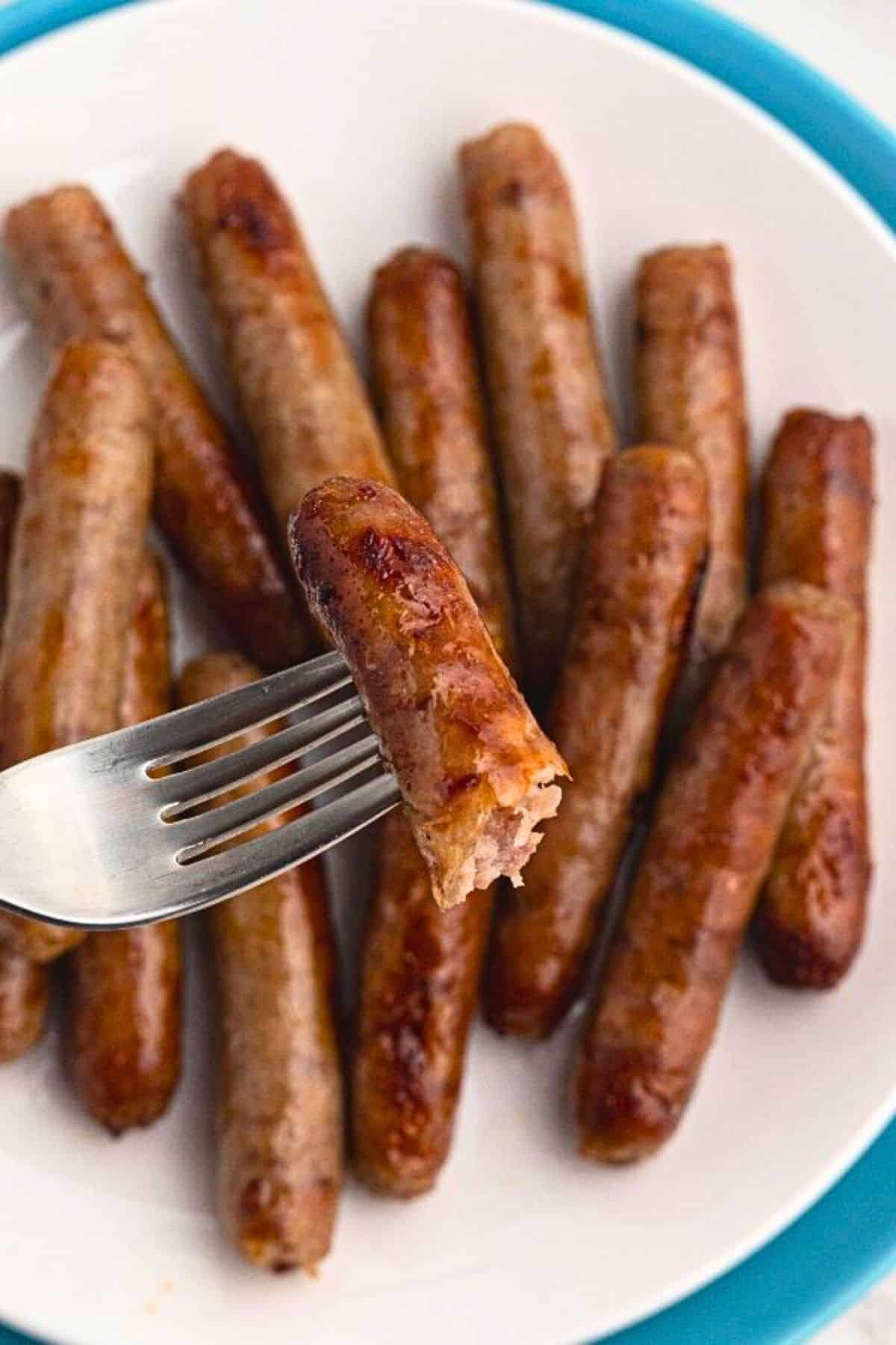 Golden sausage links cooked and stacked on a white plate, with one link on a fork. 
