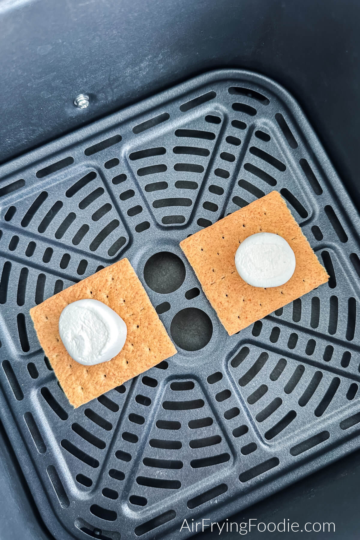 Marshmallow halved on top of graham crackers in the basket of the air fryer.