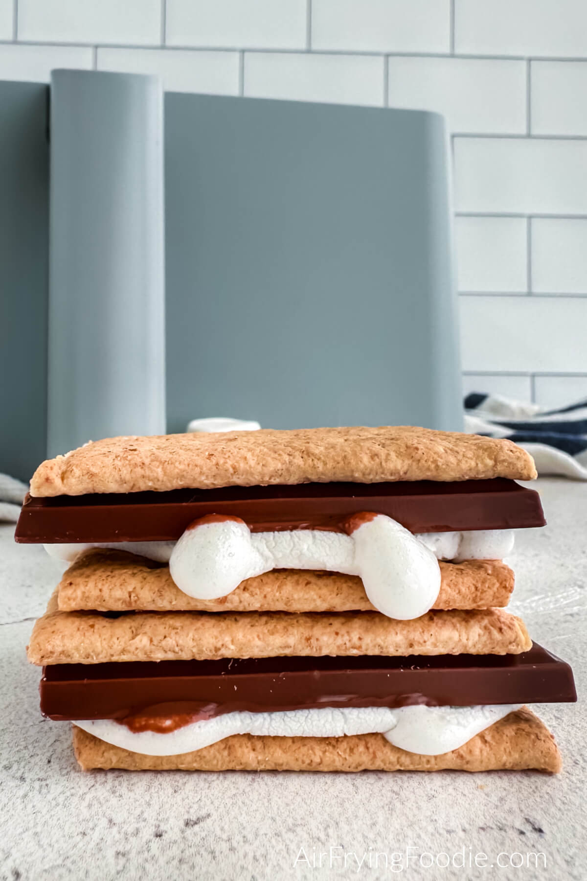 S'mores made in the air fryer, stacked on top of each other on a table with the air fryer basket in the background. 