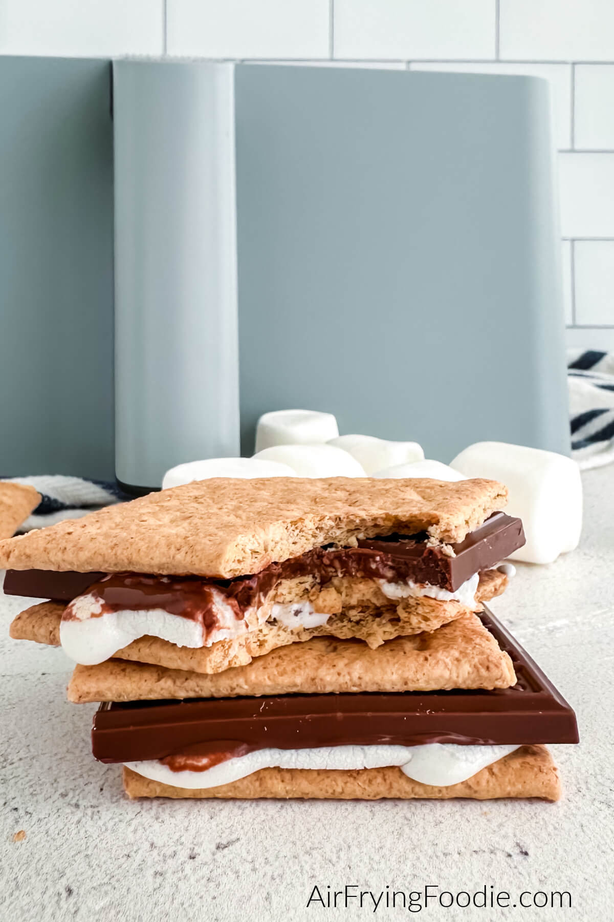 Air fryer s'mores stacked in front of an air fryer, the top one with a bite taken from it. 