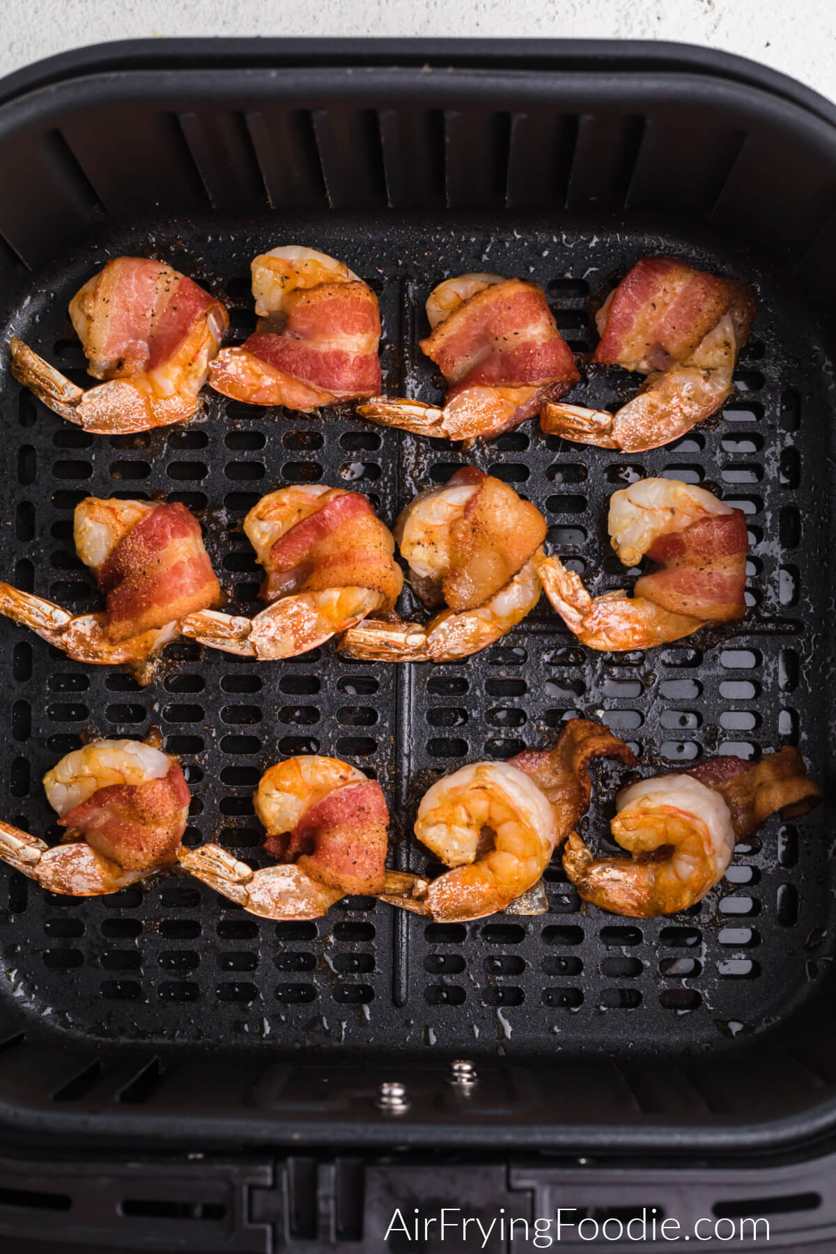 bacon wrapped shrimp in air fryer basket, cooked and ready to serve.