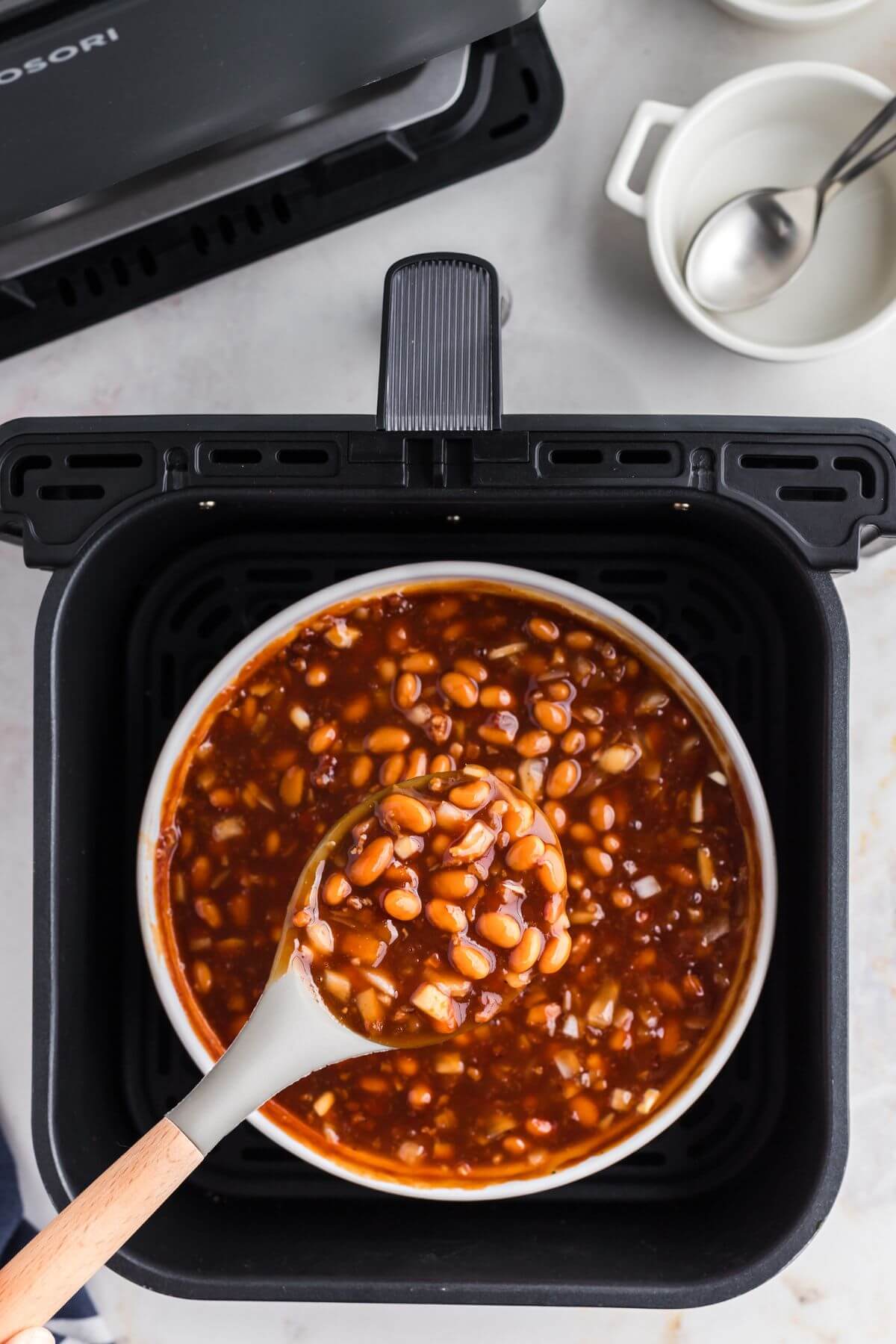 Juicy baked beans after being cooked in the air fryer, being scooped with a spoon. 