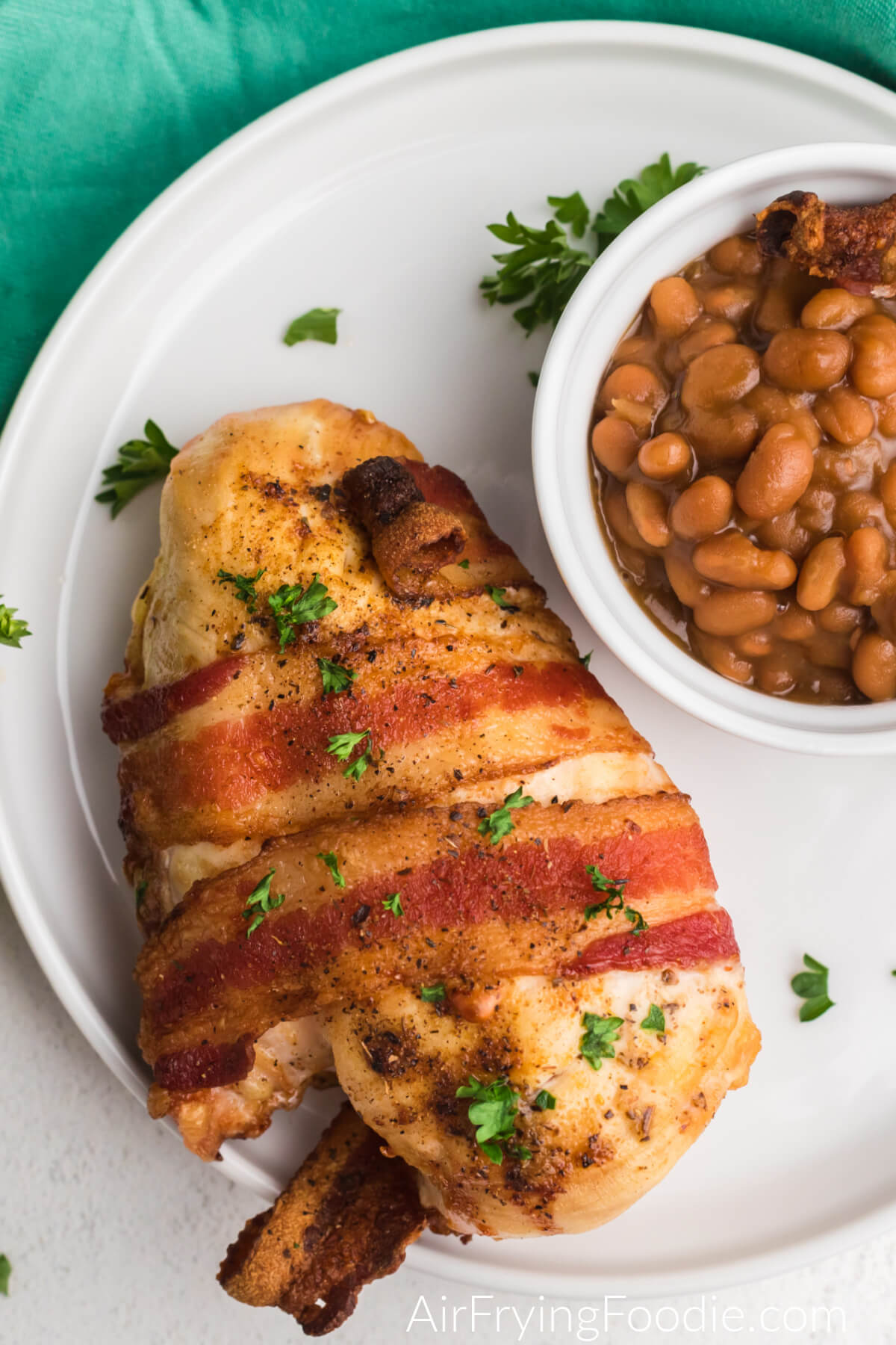 Close up of bacon wrapped chicken on a plate with a side of beans. 