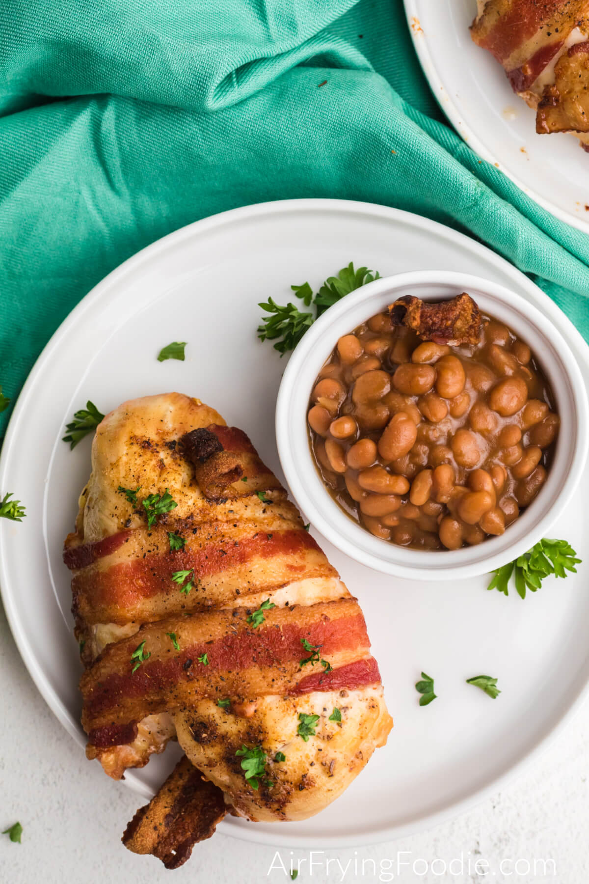 Bacon wrapped chicken on a plate with a small side bowl of beans. 