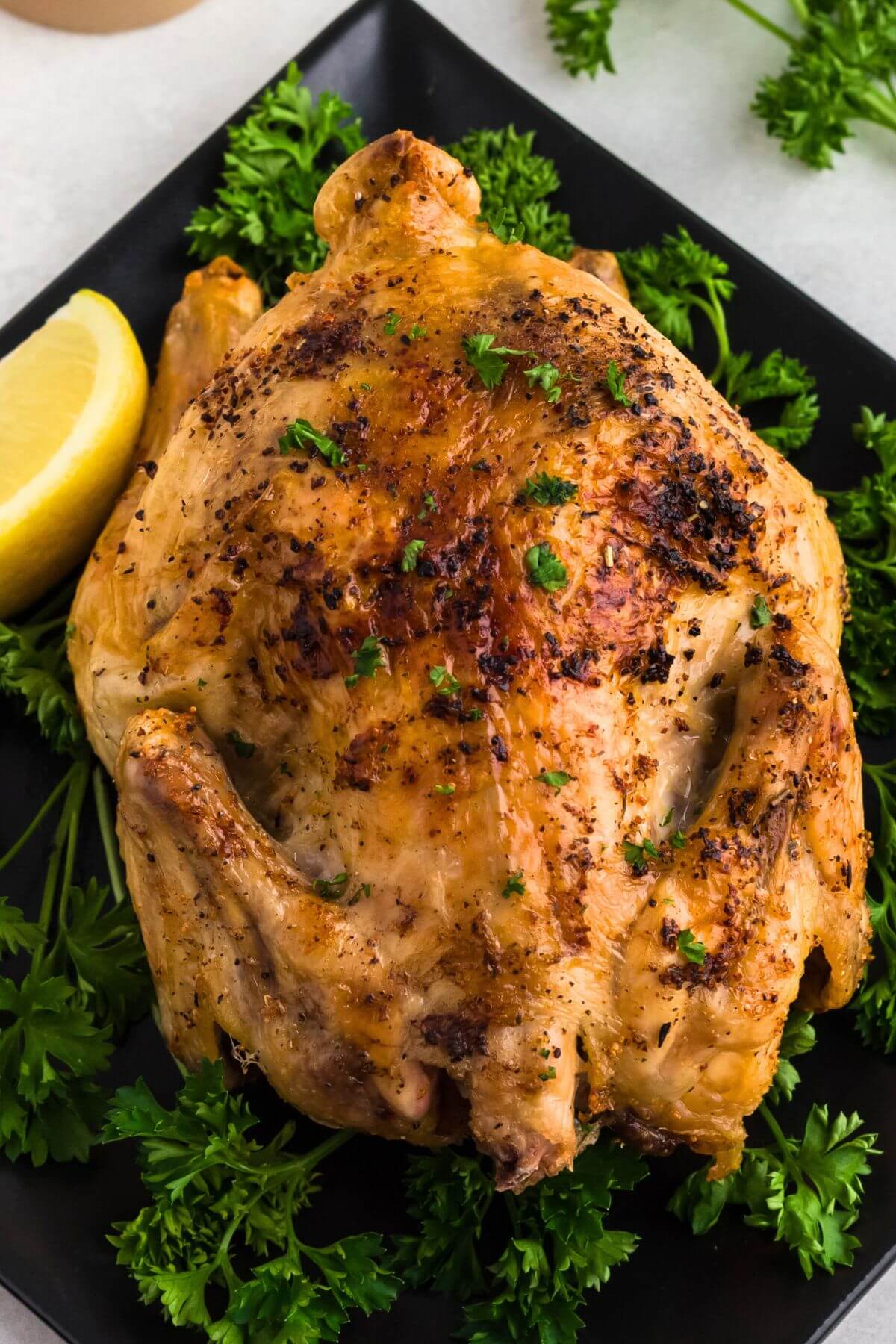 Juicy golden brown Cornish hen seasoned and served on a black plate then garnished with parsley and lemon wedges. 