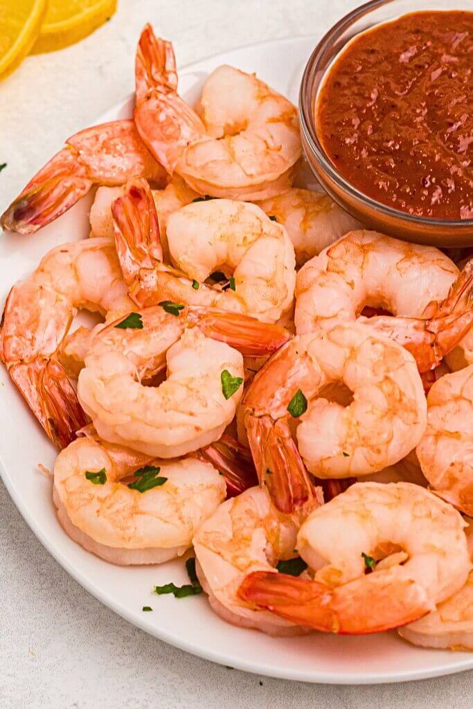 Orange juicy shrimp on a white plate with cocktail sauce. 