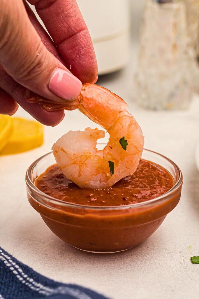 Juicy orange shrimp being dipped into cocktail sauce. 