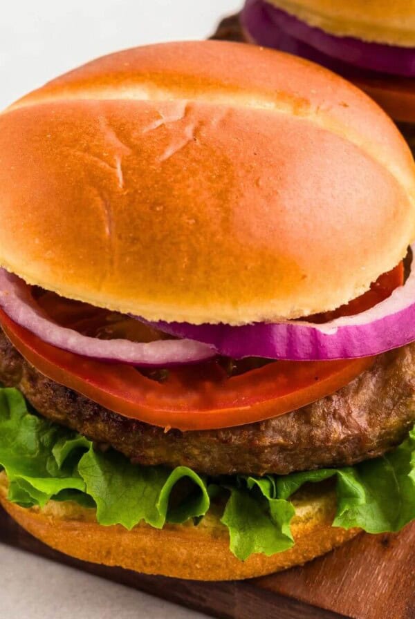 Juicy turkey burger in a bun with lettuce, tomato, and onion, on a wooden cutting board.