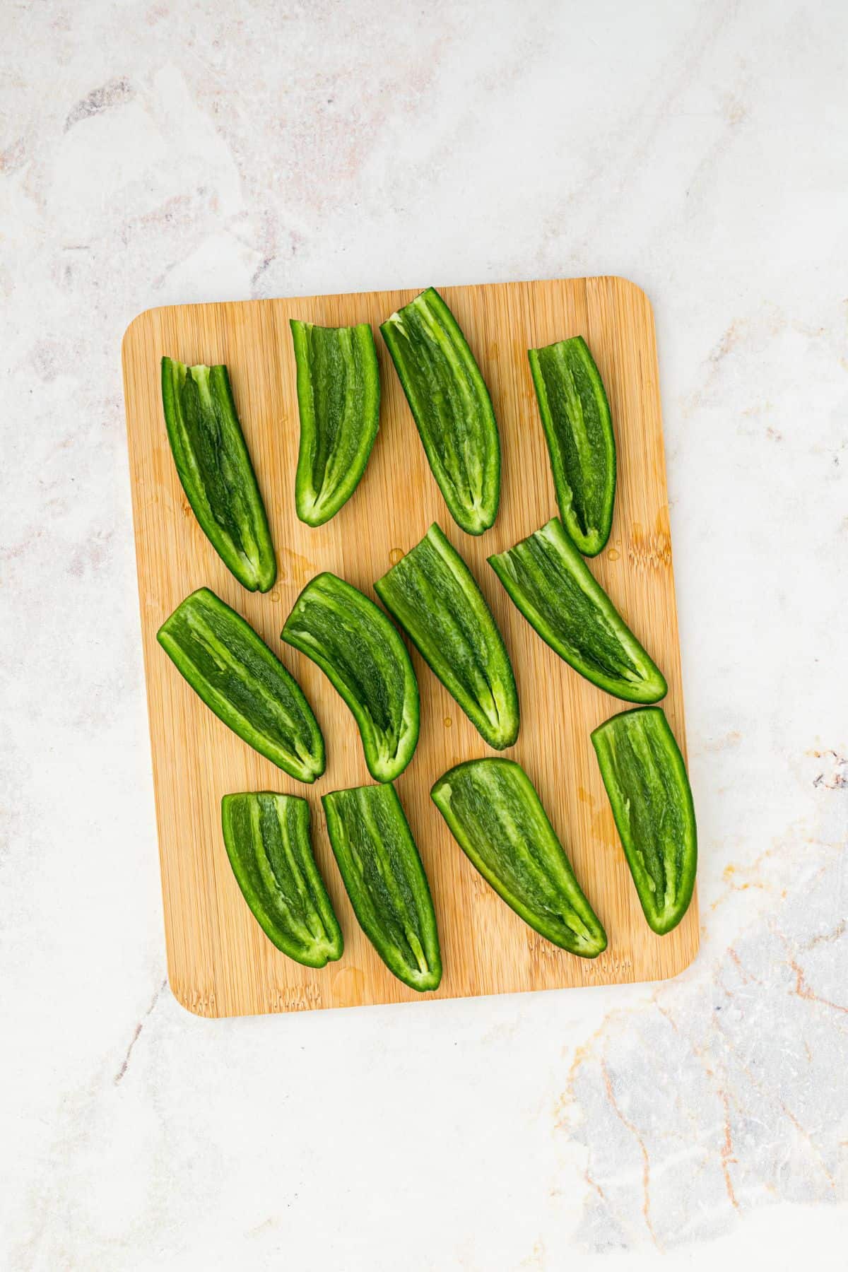 Jalapenos sliced in half with seeds and insides removed, on a wooden cutting board. 