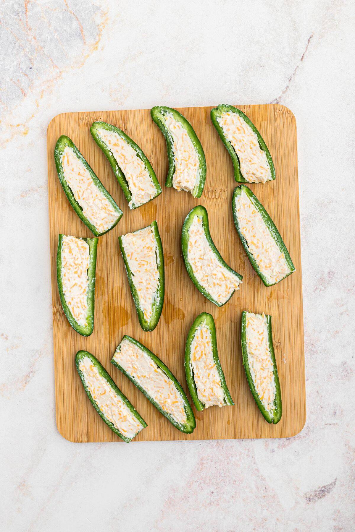 Jalapenos, sliced in half, on a wooden cutting board and filled with cheese mixture. 