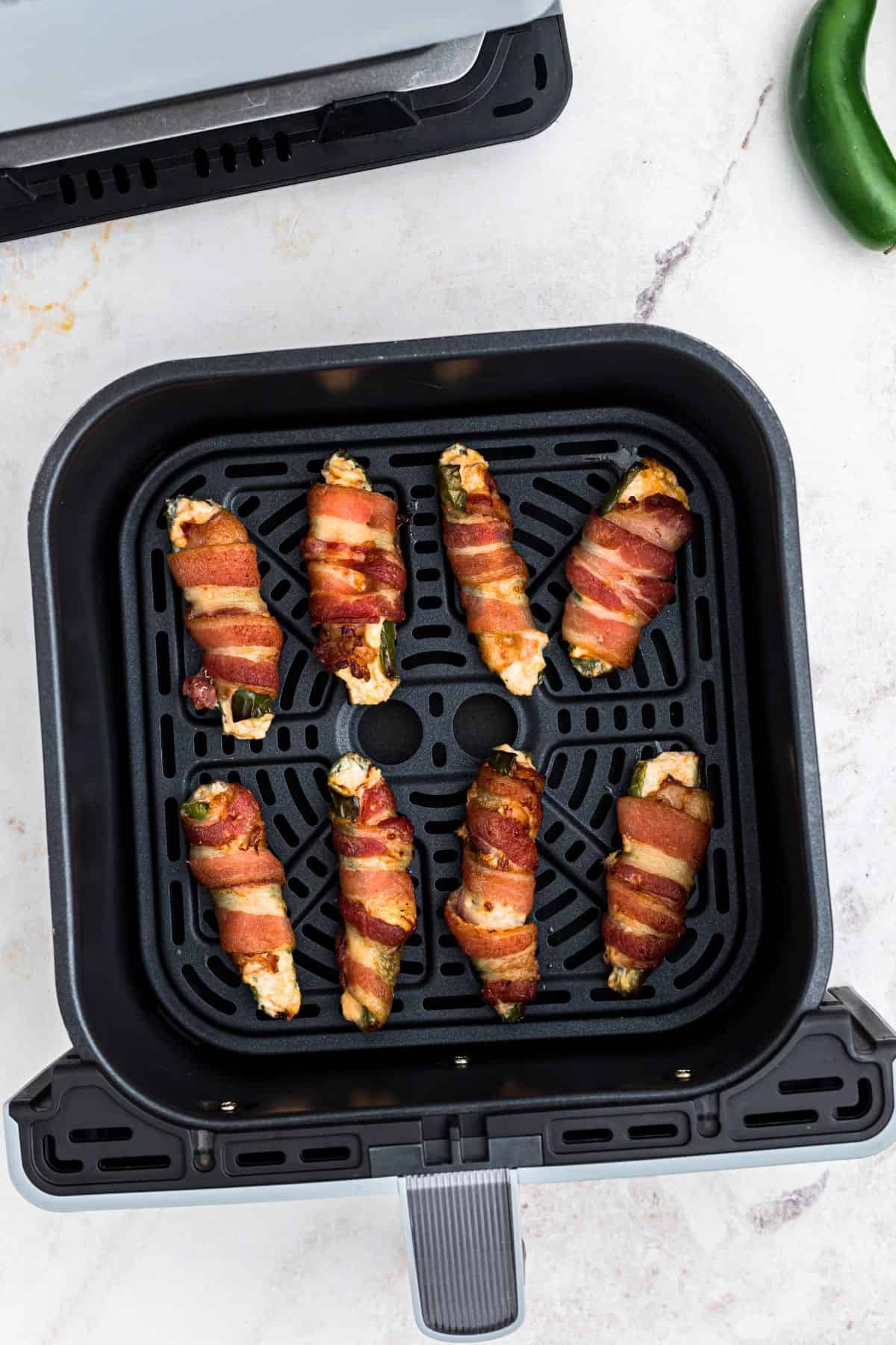 Crispy cooked jalapeno poppers in the air fryer basket, in front of an air fryer. 
