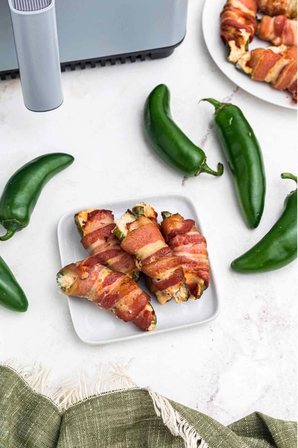 Crispy bacon wrapped jalapeno poppers on a small white square plate. 