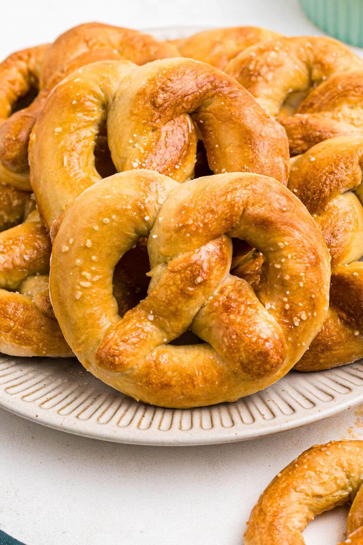 Golden brown soft pretzels on a round white plate with a bowl of melted cheese on a marble table. 